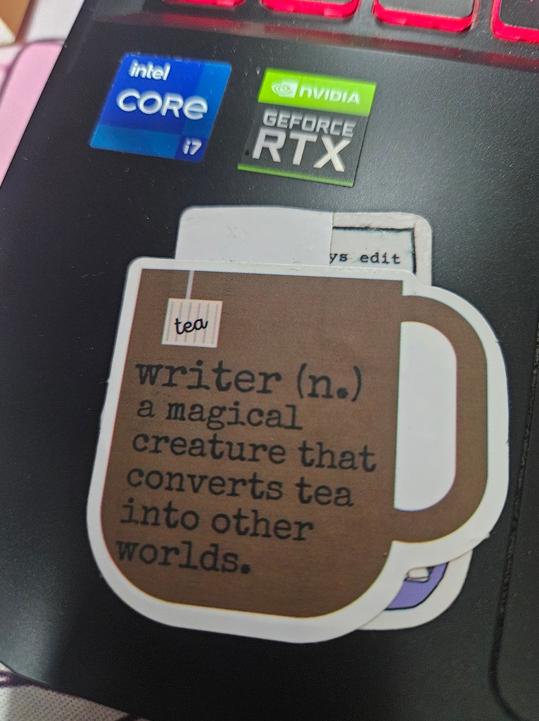 Sticker attached to laptop keyboard. Sticker says writer (n.) a magical creature that converts tea into other worlds.