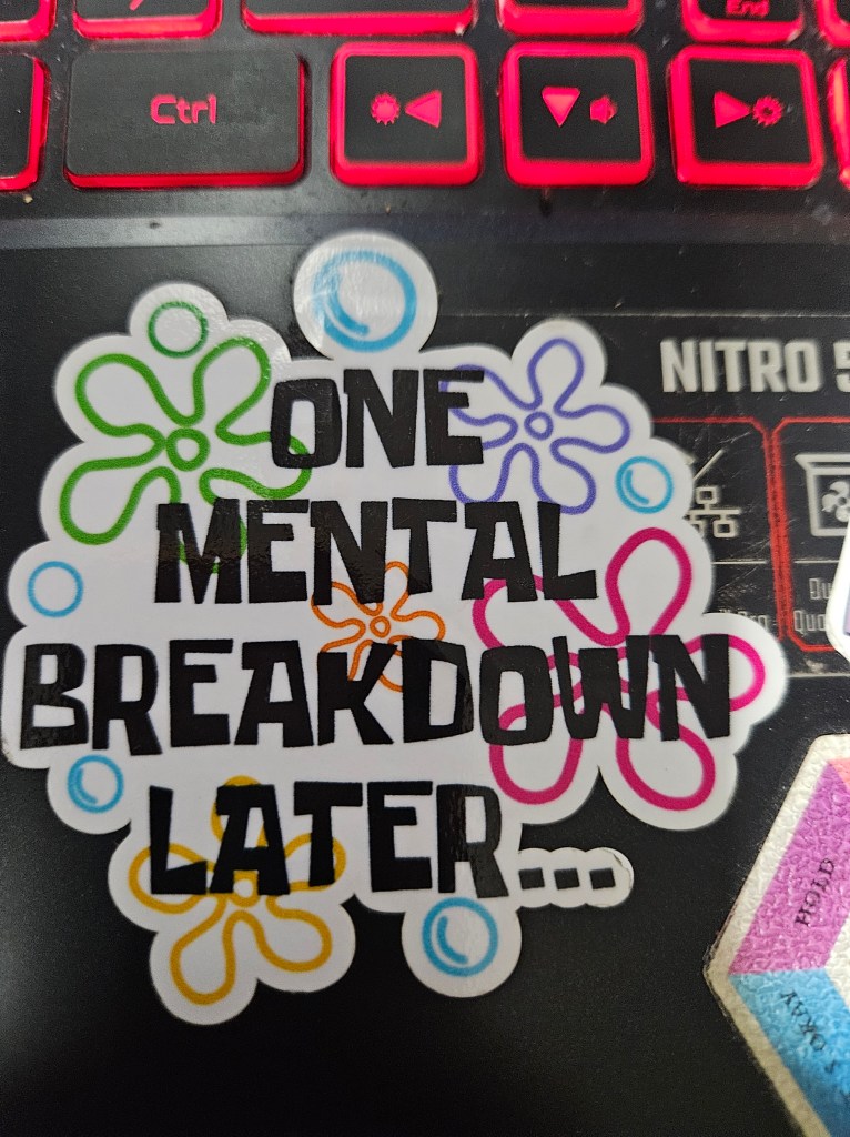 Sticker attached to laptop keyboard area. Sticker says "one mental breakdown later" 